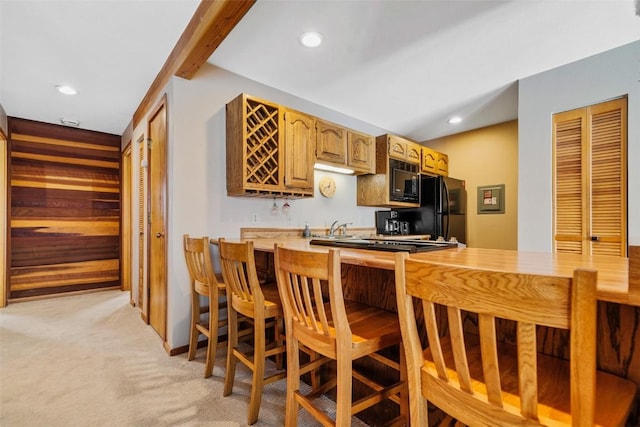 kitchen featuring beamed ceiling, kitchen peninsula, black appliances, and light carpet