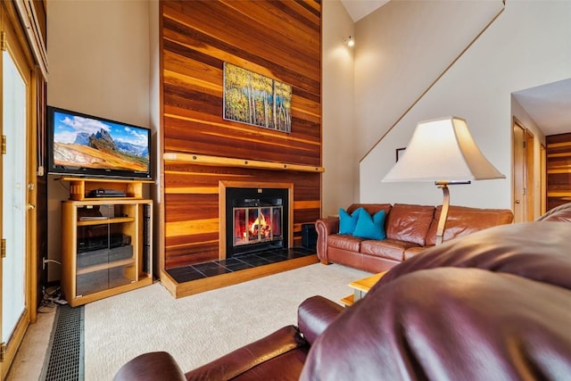 living room featuring high vaulted ceiling, wood walls, carpet floors, and a tile fireplace