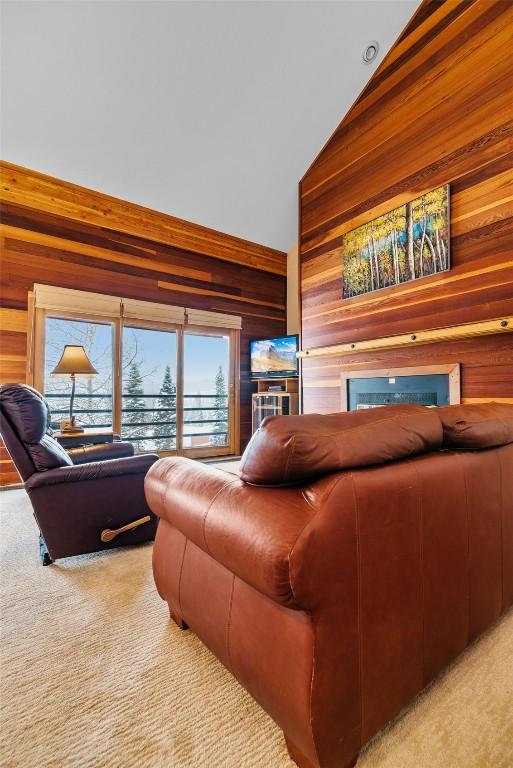 carpeted living room with lofted ceiling and wood walls