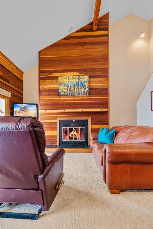 living room featuring wooden walls, carpet, and lofted ceiling with beams