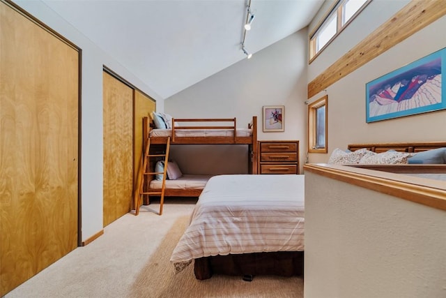 bedroom with two closets, lofted ceiling, track lighting, and light colored carpet