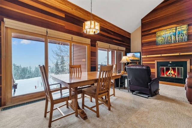 carpeted dining area featuring wood walls, lofted ceiling, and a notable chandelier