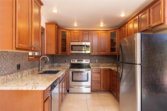 kitchen with light stone countertops, sink, decorative backsplash, light tile patterned flooring, and appliances with stainless steel finishes