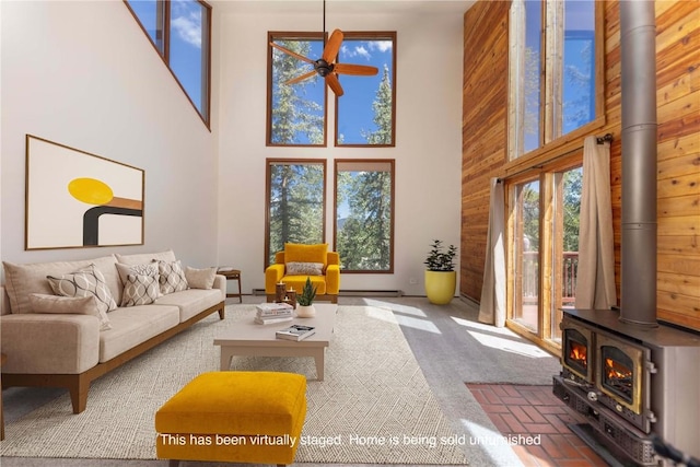 carpeted living room featuring a wood stove, ceiling fan, and a high ceiling