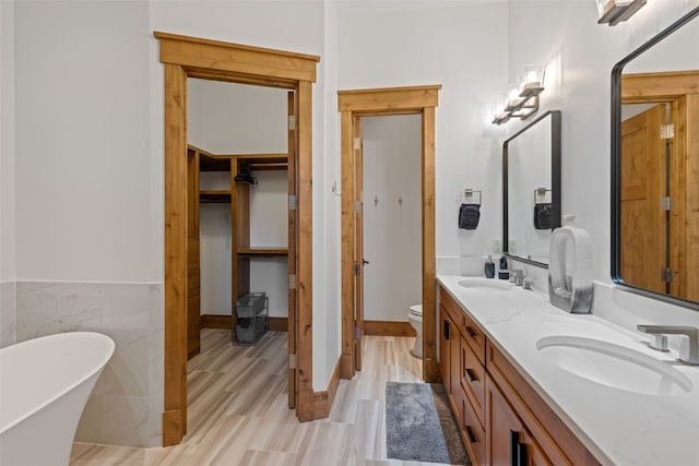 bathroom featuring a tub to relax in, vanity, tile walls, and toilet