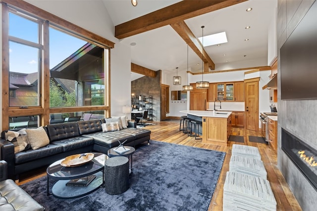 living room with a towering ceiling, light wood-type flooring, a skylight, sink, and a fireplace