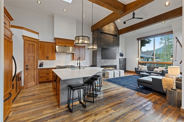 kitchen featuring beam ceiling, ceiling fan, ventilation hood, decorative light fixtures, and a tiled fireplace