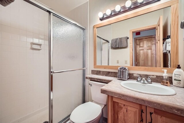 bathroom featuring vanity, a shower with door, and toilet