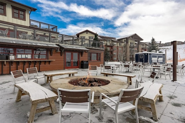 snow covered patio with a balcony, an outdoor fire pit, grilling area, and french doors