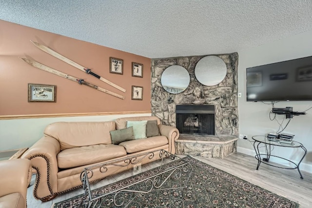 living room with hardwood / wood-style floors, a textured ceiling, and a stone fireplace