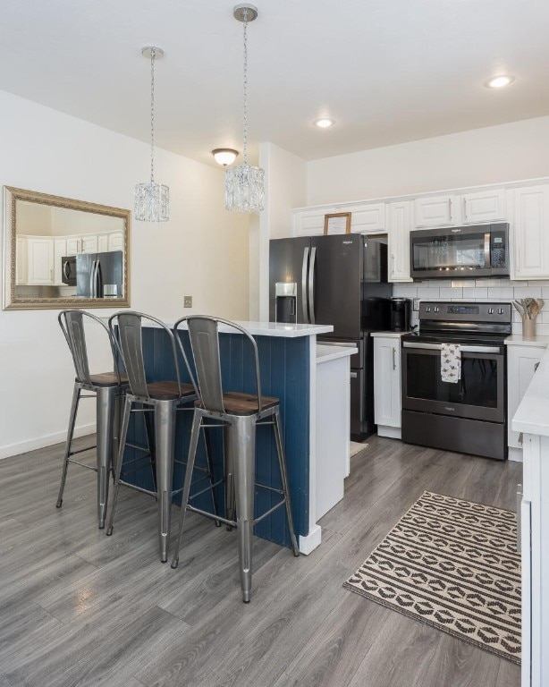 kitchen featuring stainless steel appliances, white cabinetry, hanging light fixtures, and a breakfast bar area