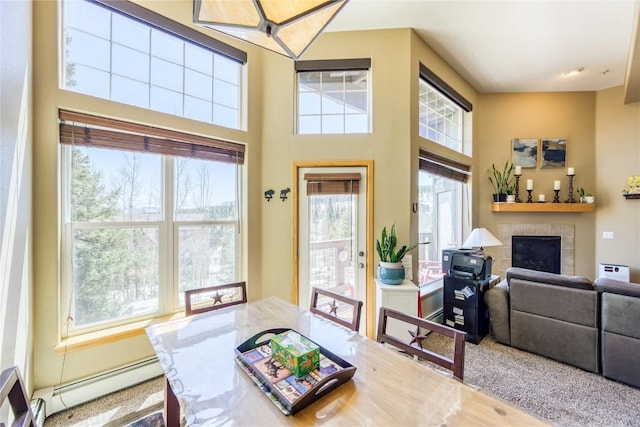dining space featuring a baseboard heating unit, a towering ceiling, and a tile fireplace