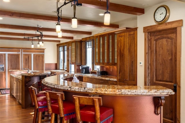 kitchen featuring light stone countertops, a kitchen island, decorative light fixtures, beam ceiling, and dark wood-type flooring