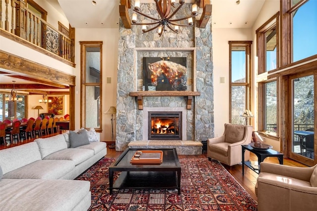 living room featuring hardwood / wood-style floors, a chandelier, high vaulted ceiling, and a stone fireplace