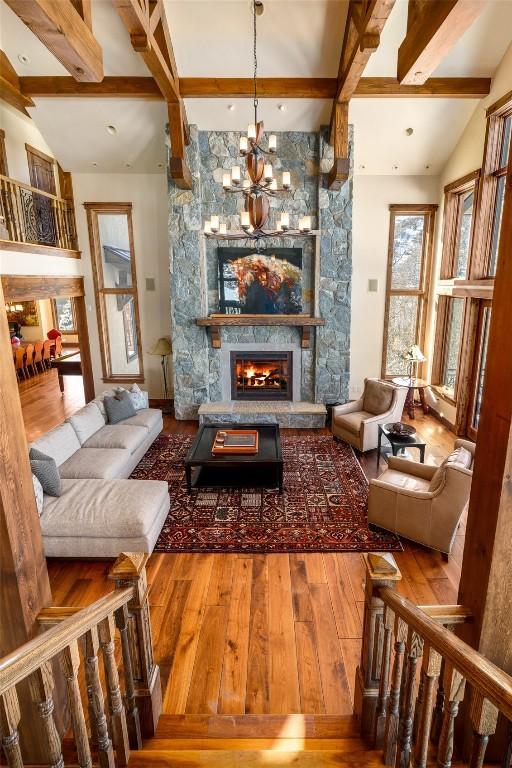 living room featuring a notable chandelier, hardwood / wood-style flooring, a fireplace, and lofted ceiling with beams