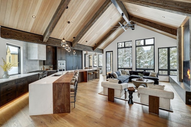 living room featuring high vaulted ceiling, sink, light wood-type flooring, beam ceiling, and wood ceiling