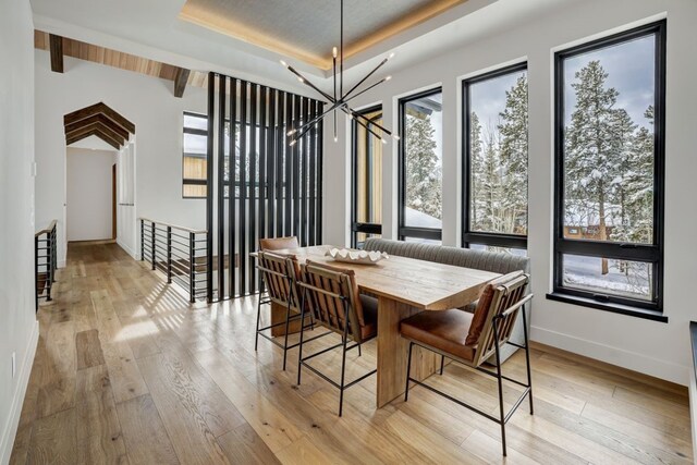 dining area featuring a notable chandelier, lofted ceiling, light wood-type flooring, and a tray ceiling