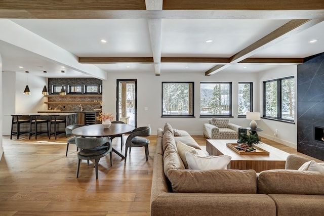 living room featuring beamed ceiling, a premium fireplace, beverage cooler, and light hardwood / wood-style flooring