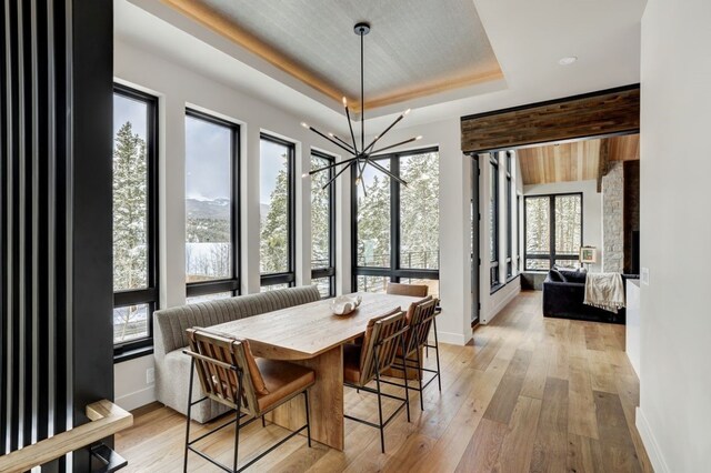 dining area with light wood-type flooring, an inviting chandelier, and a raised ceiling