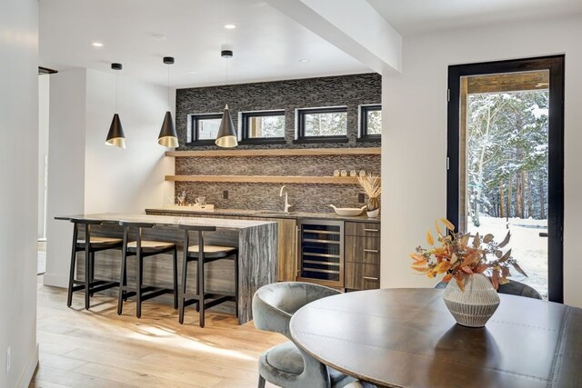 bar with backsplash, beverage cooler, sink, light hardwood / wood-style floors, and hanging light fixtures