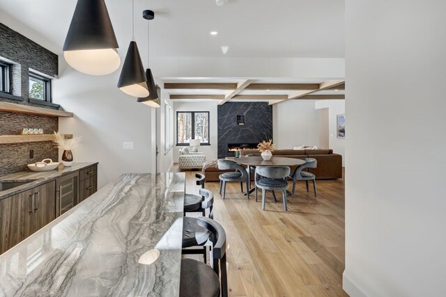 kitchen with coffered ceiling, pendant lighting, light hardwood / wood-style flooring, a premium fireplace, and beamed ceiling