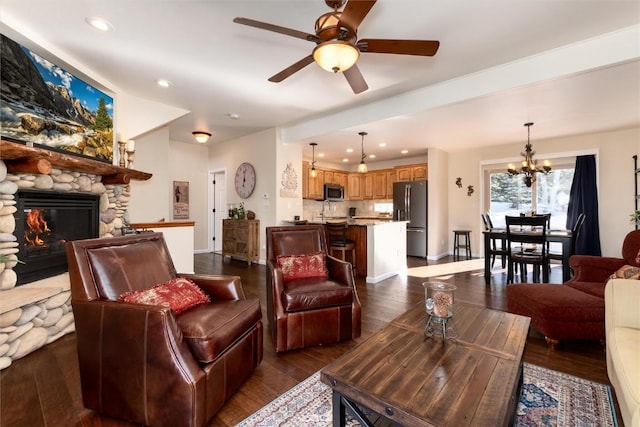 living room with dark hardwood / wood-style flooring, ceiling fan with notable chandelier, and a stone fireplace