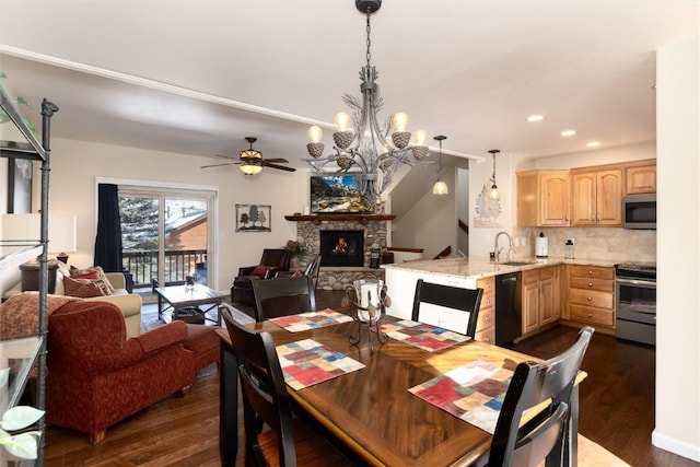 dining space with a stone fireplace, sink, ceiling fan with notable chandelier, and dark hardwood / wood-style flooring