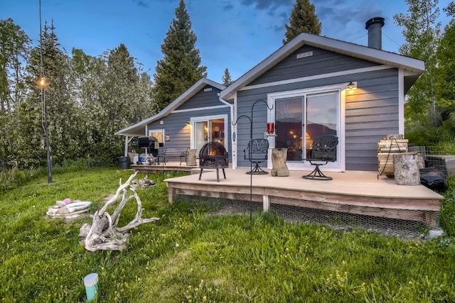 back of house featuring a wooden deck, an outdoor fire pit, and a lawn