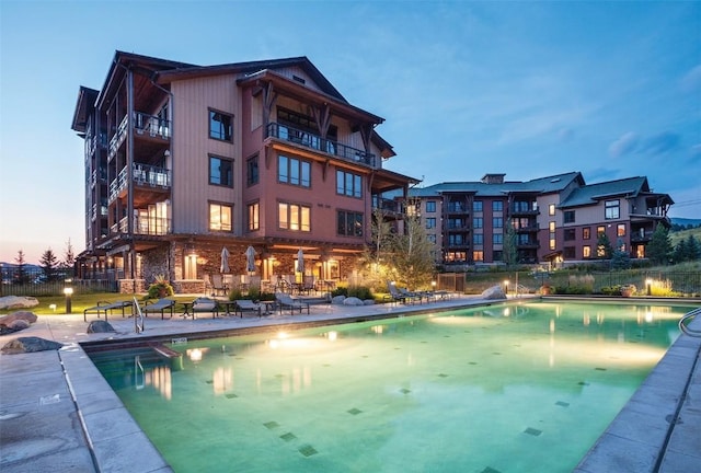 pool at dusk featuring a patio area and a community pool