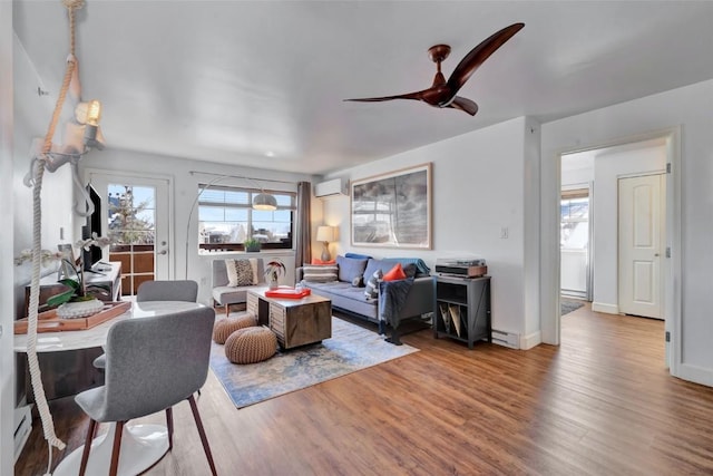 living area featuring ceiling fan, a baseboard heating unit, wood finished floors, baseboards, and an AC wall unit