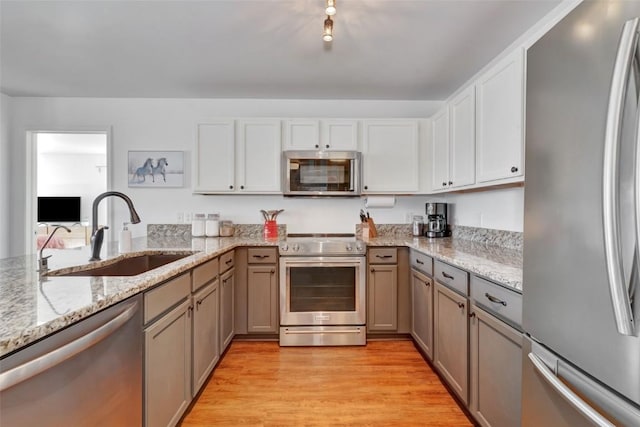 kitchen with stainless steel appliances, light wood-style floors, a sink, light stone countertops, and a peninsula