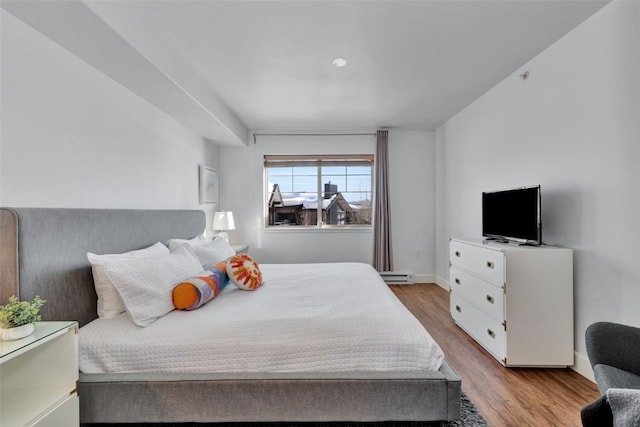 bedroom featuring baseboards, a baseboard heating unit, and wood finished floors