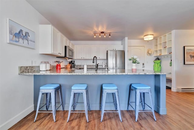 kitchen with appliances with stainless steel finishes, a kitchen breakfast bar, a peninsula, white cabinetry, and a sink