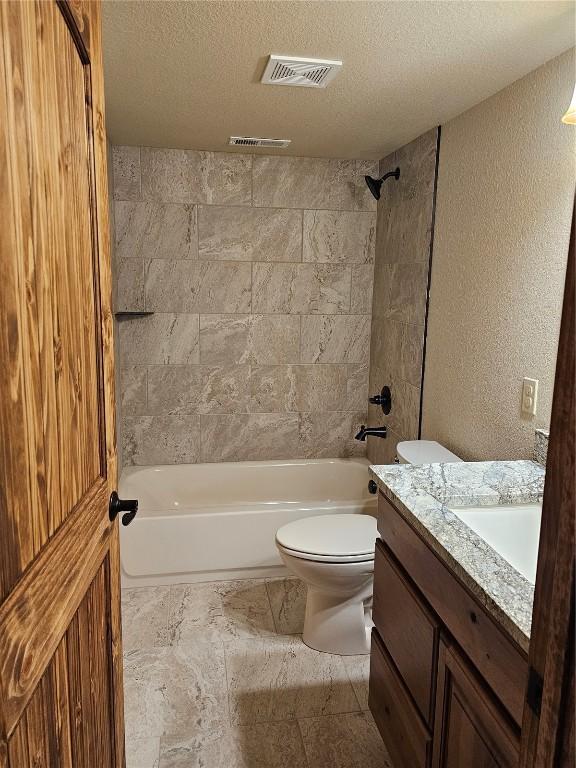 full bathroom featuring vanity, a textured ceiling, toilet, and tiled shower / bath