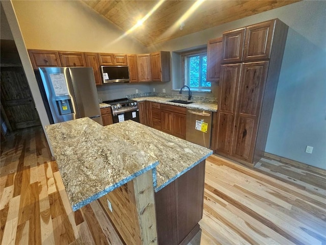 kitchen featuring light wood-type flooring, light stone counters, stainless steel appliances, vaulted ceiling, and sink