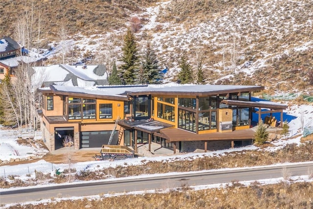 snow covered house with a wooden deck, a garage, and a sunroom