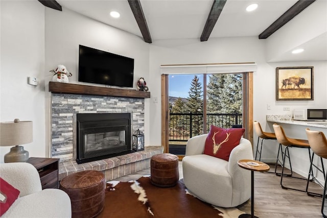 living room with beam ceiling, a stone fireplace, and light wood-type flooring