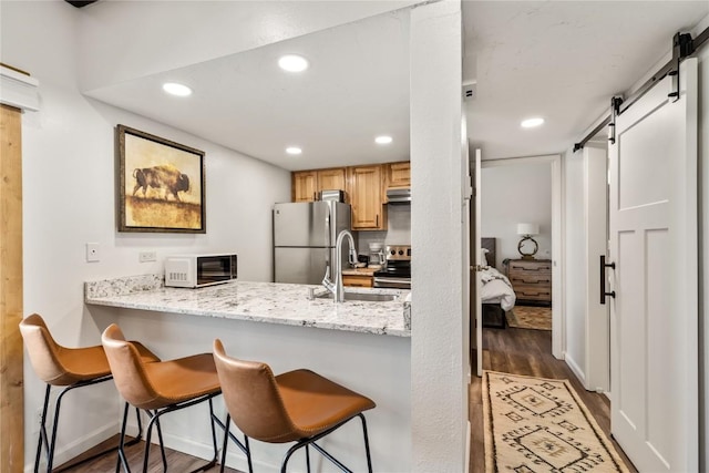 kitchen featuring sink, a barn door, dark hardwood / wood-style flooring, a breakfast bar, and appliances with stainless steel finishes