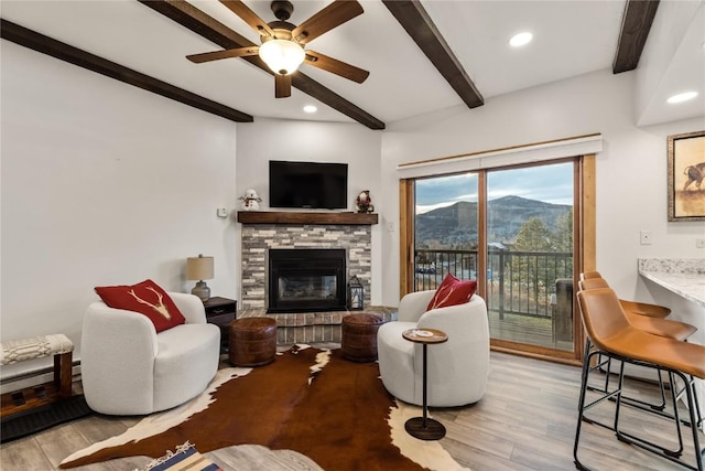 living room featuring a stone fireplace, ceiling fan, beamed ceiling, and light hardwood / wood-style floors