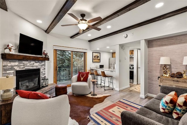 living room with beamed ceiling, ceiling fan, a stone fireplace, and hardwood / wood-style flooring