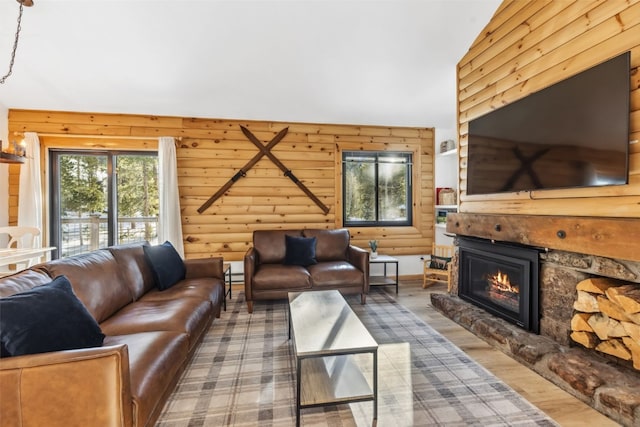 living room with log walls, hardwood / wood-style flooring, a stone fireplace, lofted ceiling, and wood walls