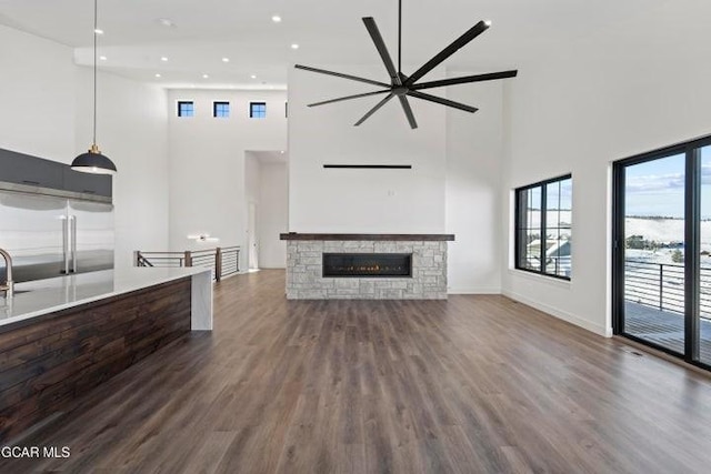 unfurnished living room featuring dark hardwood / wood-style floors, ceiling fan, a fireplace, and a high ceiling