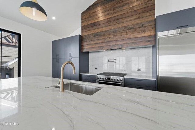 kitchen with sink, light stone counters, backsplash, lofted ceiling, and high quality appliances