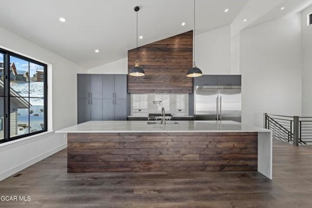 kitchen with vaulted ceiling, sink, built in refrigerator, hanging light fixtures, and an island with sink