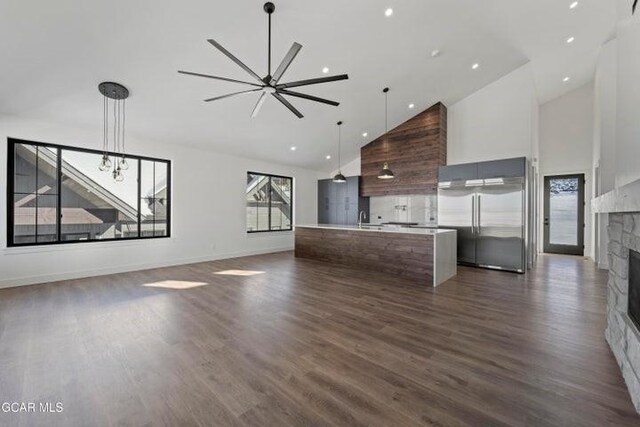 unfurnished living room featuring ceiling fan with notable chandelier, sink, high vaulted ceiling, a fireplace, and dark hardwood / wood-style floors