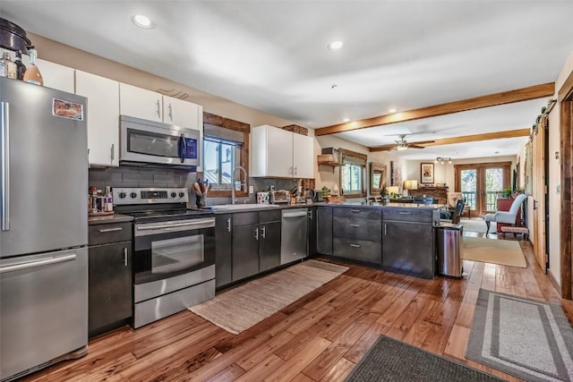 kitchen with tasteful backsplash, appliances with stainless steel finishes, white cabinets, a peninsula, and hardwood / wood-style flooring