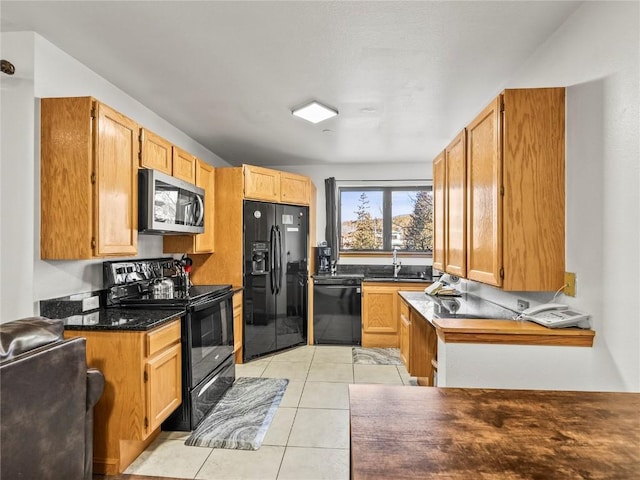 kitchen featuring dark stone countertops, sink, light tile patterned floors, and black appliances