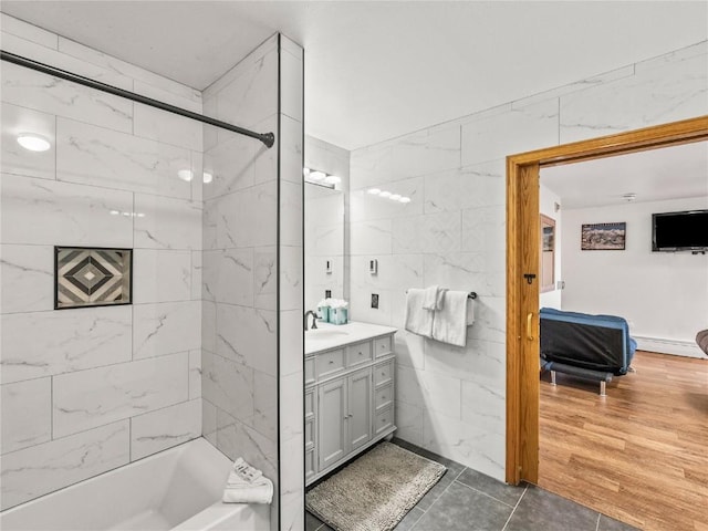 bathroom with baseboard heating, tile walls, tile patterned flooring, vanity, and tiled shower / bath