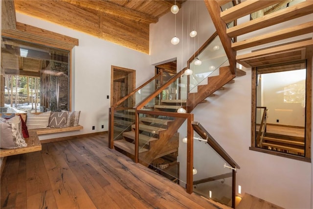 stairs with beamed ceiling, hardwood / wood-style flooring, a towering ceiling, and wood ceiling