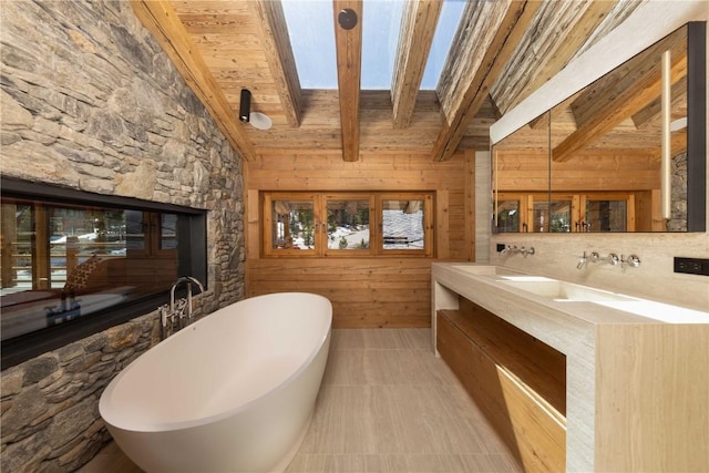 bathroom with a skylight, beam ceiling, wooden ceiling, a bathing tub, and wood walls